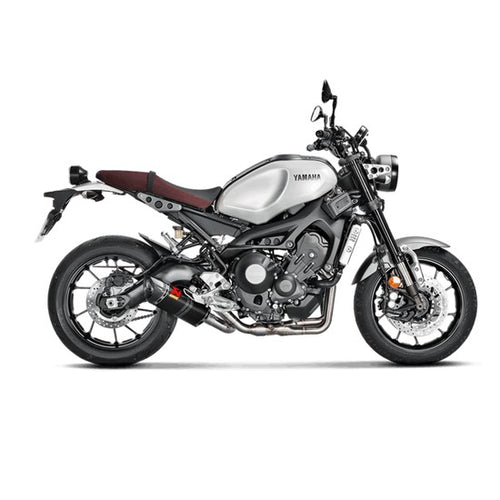 The Akrapovic Full System for Yamaha MT09/XSR900 by AKRAPOVIC is a racing exhaust with a sleek metallic finish, featuring multiple curved pipes leading to a black carbon fiber muffler adorned with a red and yellow logo.