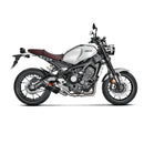 The Akrapovic Full System for Yamaha MT09/XSR900 by AKRAPOVIC is a racing exhaust with a sleek metallic finish, featuring multiple curved pipes leading to a black carbon fiber muffler adorned with a red and yellow logo.