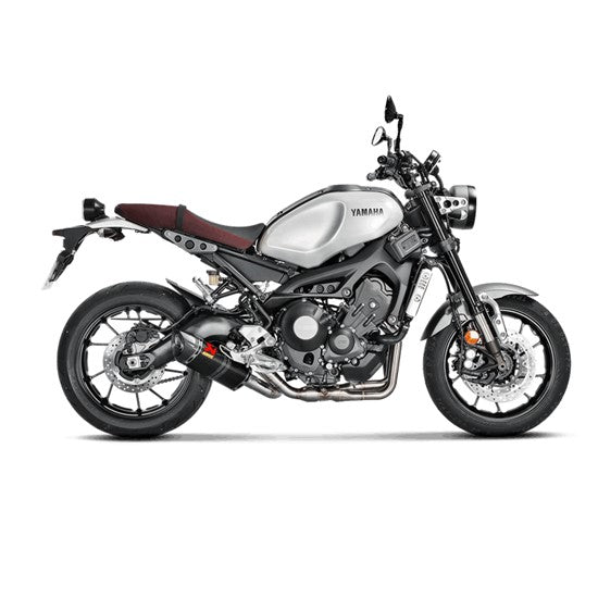 The Akrapovic Full System for Yamaha MT09/XSR900 by AKRAPOVIC is a racing exhaust with a sleek metallic finish, featuring multiple curved pipes leading to a black carbon fiber muffler adorned with a red and yellow logo.