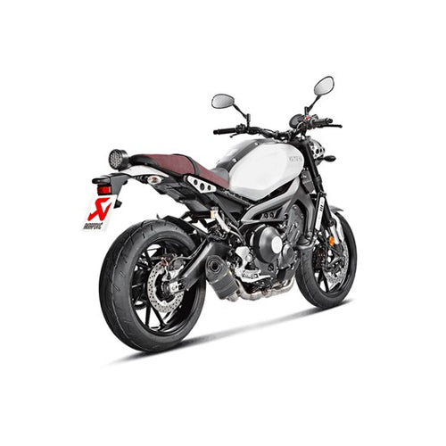 The Akrapovic Full System for Yamaha MT09/XSR900 by AKRAPOVIC is a racing exhaust with a sleek metallic finish, featuring multiple curved pipes leading to a black carbon fiber muffler adorned with a red and yellow logo.